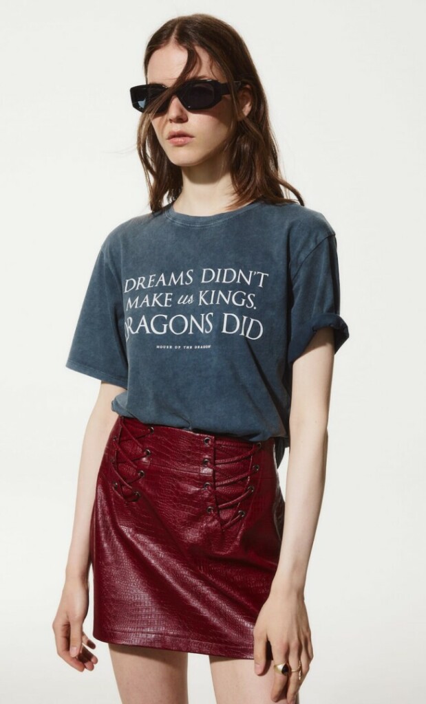 Outfit de la colección de House of the Dragon de Stradivarius, con una camiseta gris en la que se lee: "Dreams didn't make us kings. Dragons did", y una falda roja en efecto piel.